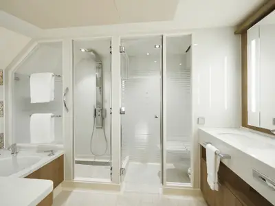 Helles, luxuriöses Badezimmer an Bord der Norwegian Bliss. Es verfügt über eine Badewanne, eine begehbare Dusche und einen eleganten Waschtisch mit beleuchtetem Spiegel. Moderne Ausstattung und neutrale Farben.