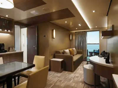 Blick in das elegant eingerichtete Wohnzimmer einer The Haven Suite an Bord der Norwegian Bliss mit Sofa, Esstisch und Balkon mit Meerblick.