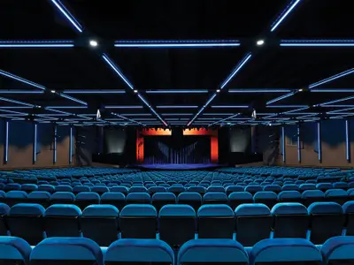 Weitwinkel des leeren Bliss Theaters an Bord der Norwegian Bliss. Blaue Sitzreihen füllen den Raum. Decke mit blauen Leuchtstreifen. Bühne ist rötlich beleuchtet.