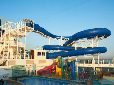 Der Aqua Park an Bord der Norwegian Bliss präsentiert aufregende blaue Wasserrutschen und einen farbenfrohen Kinderbereich. Strahlend blauer Himmel am sonnigen Tag.