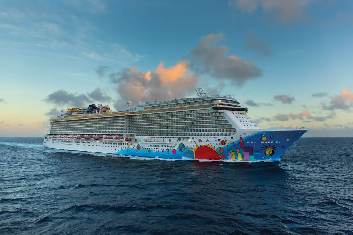 Die Norwegian Breakaway gleitet in einem dynamischen Winkel über das offene Meer. Der bunte Bug mit New Yorker Skyline-Kunst ist prominent, während der Himmel sanfte Wolken in Abendstimmung zeigt.