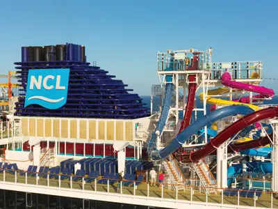 Bunte Wasserrutschen und der markante blaue NCL-Schornstein auf dem Oberdeck der Norwegian Breakaway. Einige Passagiere sind sichtbar, das Meer erstreckt sich im Hintergrund.