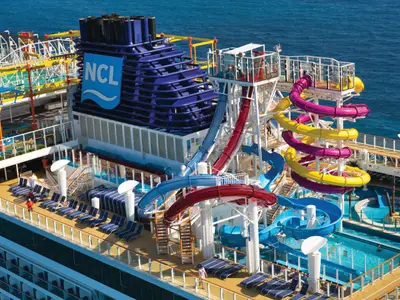 Luftaufnahme des Aqua Park der Norwegian Breakaway mit bunten Wasserrutschen, Pools, einem Seilgarten und dem NCL-Logo auf dem Schornstein auf See.
