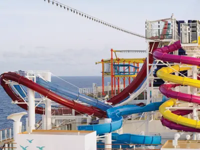 Auf dem AquaPark der Norwegian Breakaway schlängeln sich rote, blaue, gelbe und pinke Wasserrutschen über mehrere Decks vor dem weiten Blau des Meeres und Himmels.