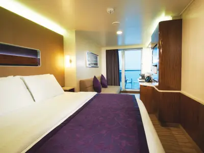 Helle Balkonkabine an Bord der Norwegian Breakaway mit Doppelbett, bequemer Couch und TV-Bereich. Eine große Glastür führt zu einem Balkon mit weitem Meerblick.