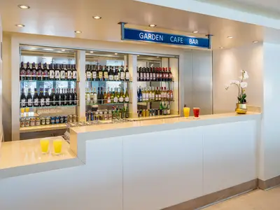 Blick auf die Theke der Garden Cafe Bar an Bord der Norwegian Breakaway, gefüllt mit Wein-, Spirituosen- und Bierflaschen. Zwei gelbe und ein rotes Getränk stehen auf der Theke neben einer Orchidee.