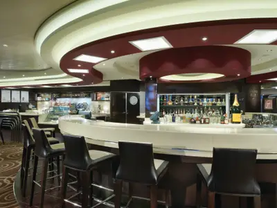 Blick in die moderne Atrium Bar & Cafe an Bord der Norwegian Breakaway. Eine geschwungene Bar mit Getraenken und Hockern, dahinter der Cafe-Bereich.