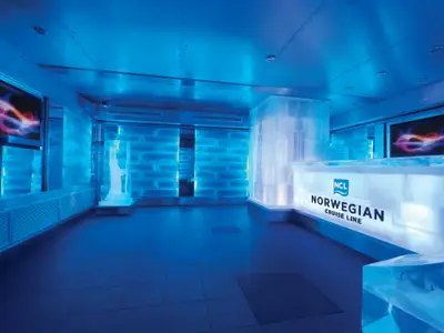 Die blaue Ice Bar an Bord der Norwegian Breakaway. Eiswände, beleuchtete Bar mit NCL-Logo und Bildschirme. Eine Eisskulptur. Modernes Ambiente.