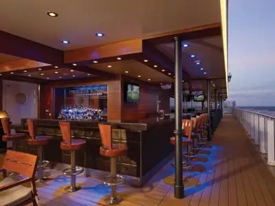 An Bord der Norwegian Breakaway: Maltings Bar auf dem Außendeck. Abendstimmung. Blaue Bodenlichter, leere Barhocker am Tresen mit Flaschen. Blick auf das offene Meer.