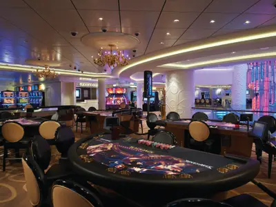 Das moderne Casino der Norwegian Breakaway zeigt leere Blackjack-Tische. Im Hintergrund sind Spielautomaten und eine beeindruckende farbige Lichtinstallation zu sehen.