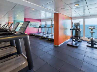 Das moderne Fitnesscenter der Norwegian Breakaway. Es zeigt mehrere Laufbaender und Fitnessgeraete mit Meerblick. Die Waende sind farbenfroh gestaltet.