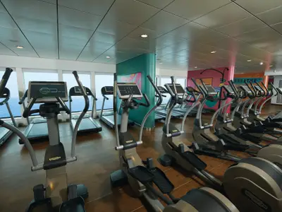 Das helle Fitnesscenter an Bord der Norwegian Breakaway bietet eine Reihe von Technogym-Ergometern und Laufbändern mit grossen Fenstern, die einen weiten Blick auf das offene Meer ermöglichen. Die Wände sind mit farbenfroher Street-Art-ähnlicher Kunst verziert.