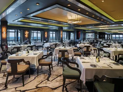 Das luxuriöse Spezialitätenrestaurant Cagney's Steakhouse an Bord der Norwegian Breakaway bei Tag. Es zeigt Tische, Stühle und grosse Fenster mit Meerblick.