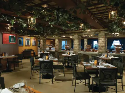 Innenansicht des italienischen Spezialitätenrestaurants La Cucina an Bord der Norwegian Breakaway. Mit Steinmauern, grünen Ranken an der Decke und zahlreichen Holztischen.