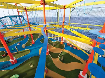 Blick von oben auf das Sportdeck der Norwegian Breakaway mit farbenfrohem Seilgarten und Minigolfanlage vor blauem Meer. Mehrere Personen sind bei den Aktivitäten zu sehen.