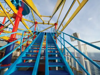 Norwegian Breakaway: Farbenfroher Ropes Course mit blauen Treppen, gelben Balken, roten Stützen. Meer und Himmel im Hintergrund. Aktives Erlebnis an Deck.