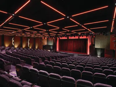 Theater an Bord der Norwegian Breakaway. Leere violette Sitze führen zur Bühne mit roten Vorhängen. Moderne rote Lichtinstallationen an der Decke.