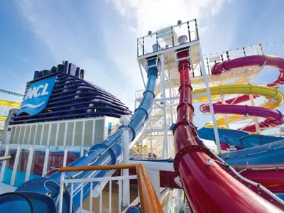 Weitwinkelaufnahme der farbenfrohen Wasserrutschenanlage und des markanten blauen NCL-Schornsteins an Bord der Norwegian Breakaway unter strahlendem Himmel. Ohne Personen.