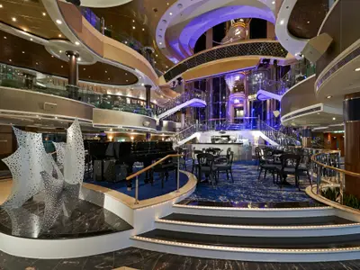 Das imposante Atrium der Norwegian Dawn mit Flügel, Bar, Treppen und Kunstskulpturen bei Abendstimmung.