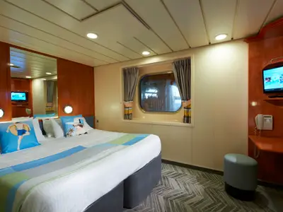 Helle Aussenkabine an Bord der Norwegian Dawn. Ein Doppelbett mit bunten Kissen, ein rundes Fenster mit Vorhängen und Meerblick, Flachbild-TV, Telefon und Schreibtisch. Modernes, gemütliches Dekor.