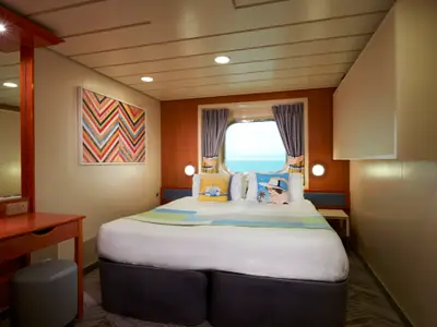Helle Aussenkabine der Norwegian Dawn mit Doppelbett, Bullauge und Meerblick. Links ein Schminktisch und ein modernes Kunstwerk. Modern und gemütlich.