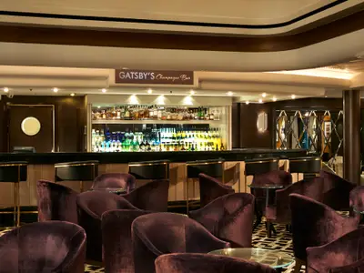 Elegante Gatsby's Champagne Bar an Bord der Norwegian Dawn mit samtbezogenen Sitzen und beleuchteter Spirituosenwand.
