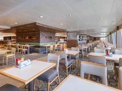 Das helle und weitläufige Buffetrestaurant GardenCafe an Bord der Norwegian Dawn, mit vielen Tischen, gepolsterten Bänken und Blick auf das Meer durch große Fenster.