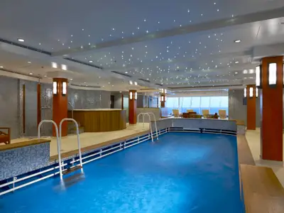 Moderner Indoor-Pool der Norwegian Dawn mit blauem Becken, Holz-Whirlpool und Meerblick. Die Decke ist mit Sternenlichtern und Spots versehen.