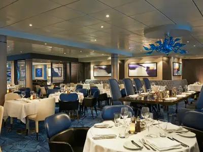 Blick in das elegant gestaltete Restaurant Aqua an Bord der Norwegian Dawn. Blaue Stühle, weiss gedeckte Tische und eine blaue Glas-Lichtinstallation an der Decke prägen den modernen Raum.