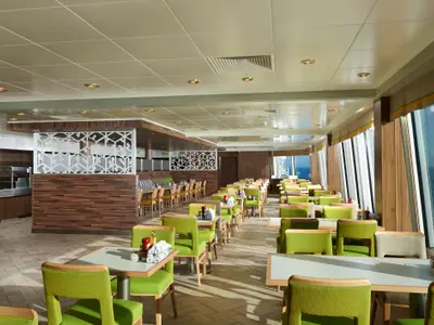 Helles und geräumiges Buffet-Restaurant Garden Café an Bord der Norwegian Dawn. Reihen von Tischen mit hellgrünen Stühlen sind bereit für Gäste, große Fenster bieten Meerblick.
