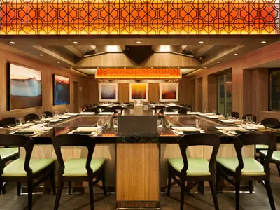 Das Teppanyaki-Restaurant an Bord der Norwegian Dawn ist elegant. Es zeigt gedeckte Tische, hellgrüne Stühle, Holzwände, Kunstwerke und eine markante Deckenbeleuchtung.