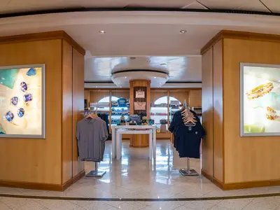 Der Duty-Free-Shop der Norwegian Dawn. Beleuchtete Schaukästen zeigen Schmuck. Kleiderständer und ein Tisch präsentieren Kleidung und Souvenirs.