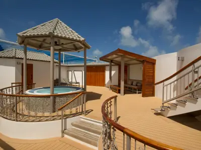 Sonnendeck der Norwegian Dawn: Whirlpool unter Pavillon, überdachte Lounge. Elegante Treppen und helle Holzdetails prägen das luxuriöse Ambiente unter blauem Himmel.