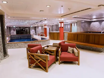 Umfassender Spa-Bereich an Bord der Norwegian Dawn, mit einem langen Lap Pool, einem Whirlpool, roten Lounge-Sesseln und eleganten Fliesenwänden.