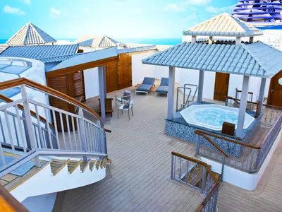 Luxuriöser Outdoor-Bereich an Bord der Norwegian Dawn. Ein sprudelnder Whirlpool unter einem Dach, umgeben von Holzdecks, Liegestühlen und privaten Hütten mit Meerblick.