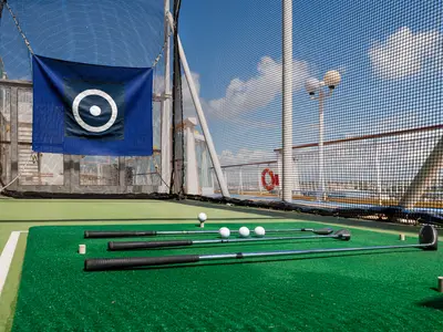 Ein Golfabschlagnetz an Bord der Norwegian Dawn mit mehreren Golfschlägern, Bällen und einer Zielscheibe auf einem Kunstrasen-Abschlagbereich.