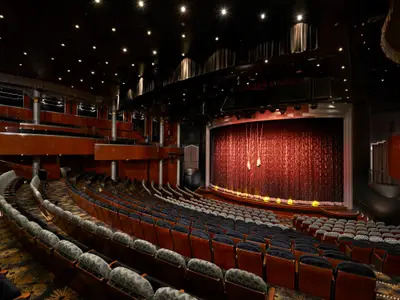 Das Stardust Theater an Bord der Norwegian Dawn zeigt die leeren Sitzreihen und die Bühne mit geschlossenem rotem Vorhang, bereit für eine Vorstellung. Die dunkle Holzvertäfelung und die gedämpfte Beleuchtung schaffen eine klassische Abendstimmung.