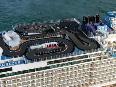 Luftaufnahme der Norwegian Encore zeigt die weitläufige Go-Kart-Rennstrecke auf dem Oberdeck, umgeben von Wasserrutschen und weiteren Freizeitanlagen. Das Meer ist im Hintergrund sichtbar.