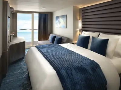 Moderne Balkonkabine der Norwegian Encore. Ein grosses Bett mit blauen Kissen und Tagesdecke. Fensterfront mit Meerblick. Dazu ein Sofa und eine TV-Konsole.