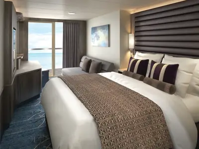 Moderne Balkonkabine an Bord der Norwegian Encore. Komfortables Bett, Schlafcouch, TV und Meerblick. Elegantes Design in warmen Brauntönen und blauem Teppich.