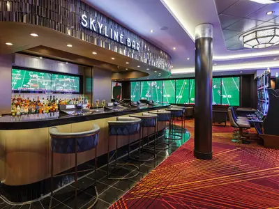 Die moderne Skyline Bar an Bord der Norwegian Encore. Gut bestückte Bar mit Hockern, große Bildschirme zeigen Sport. Rechts mehrere Spielautomaten.