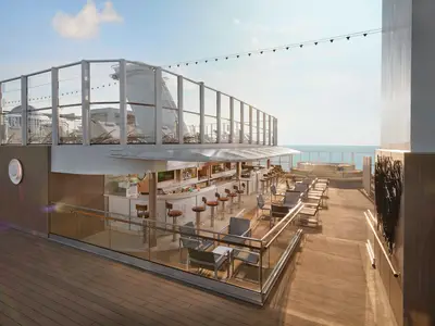 Moderne, offene Bar-Lounge mit vielen Hockern und Sitzgelegenheiten auf dem Sonnendeck der Norwegian Encore. Darüber liegt ein weiteres Deck mit Liegestühlen und Meerblick.