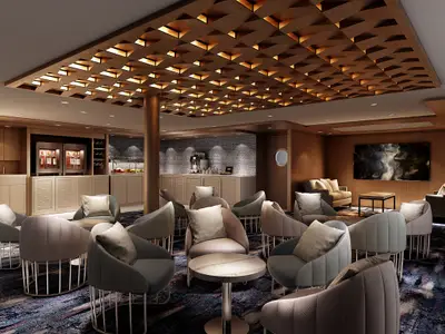 Blick in die moderne Studio Lounge an Bord der Norwegian Encore mit eleganten Sitzgruppen, Bar und Holzakzenten. Die Decke ist mit geometrischen Holzelementen und integrierten Lichtern gestaltet.
