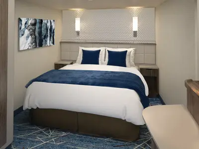 Moderne Innenkabine an Bord der Norwegian Encore. Das Doppelbett mit blauen Kissen und Bettlaeufer steht im Mittelpunkt. Ein abstraktes Kunstwerk und Nachttische runden das Bild der komfortablen Unterkunft ab.
