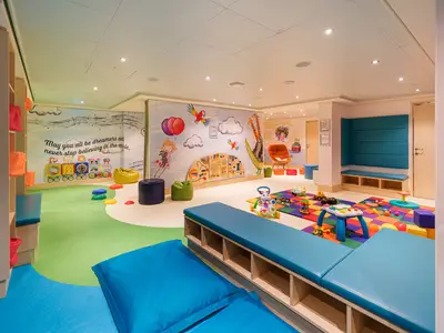 Der bunte Kinderbereich "Guppies" an Bord der Norwegian Encore. Er zeigt eine weite Ansicht des Raumes mit Spielzeugen, gepolsterten Bänken und Bean Bags, sowie liebevollen Wandmalereien.