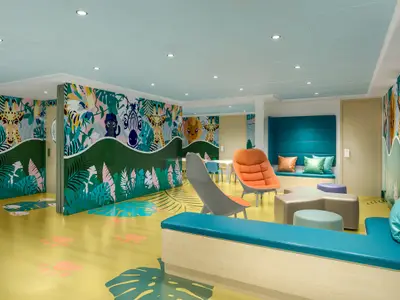 Detailaufnahme des lebhaften Kinderbereichs Guppies an Bord der Norwegian Encore. Die Wände sind mit Dschungeltieren und Blättern bemalt. Gelber Boden mit bunten Pfotenabdrücken. Moderne Sitzgelegenheiten in leuchtenden Farben.