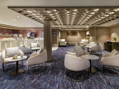 Die Studio Lounge der Norwegian Encore mit modernen Sesseln, Tischen, einem Buffet im Hintergrund und einer stilvollen Deckenbeleuchtung.