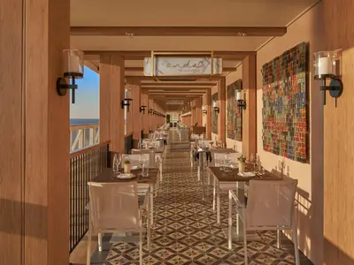 Elegantes Onda by Scarpetta Restaurant an Bord der Norwegian Encore. Der lange Raum mit warmen Holztönen und gedeckten Tischen bietet Meerblick an der Seite.