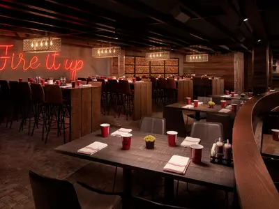 Das Q Texas Barbeque Restaurant an Bord der Norwegian Encore. Dunkle Holztische, rote Becher und weiss-rote Servietten. Ein leuchtender Neonschriftzug "Fire it up" und rustikale Holzwände prägen die moderne und gemütliche Atmosphäre.