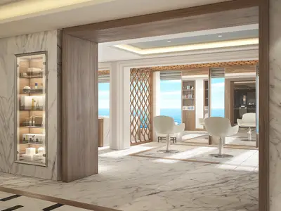 Blick in den luxuriösen Schönheitssalon der Norwegian Encore mit mehreren Friseurstühlen und großen Fenstern zum Meer. Links beleuchtete Produktvitrinen. Marmorboden.